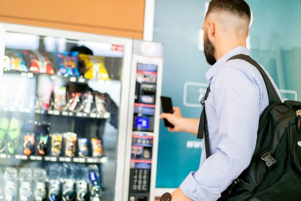 Man using mobile phone to make a contactless payment at a snack vending machine in a public space